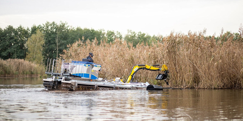 Truxor Harvester Removing Dense Aquatic Vegetation Along Wetland Shoreline Using Dredging Attachment